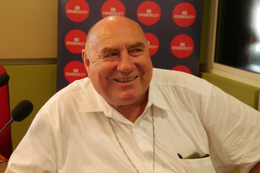 A man in a white shirt sits smiling