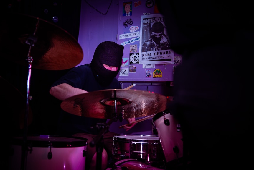 Drummer wearing all black and wearing a mask. 