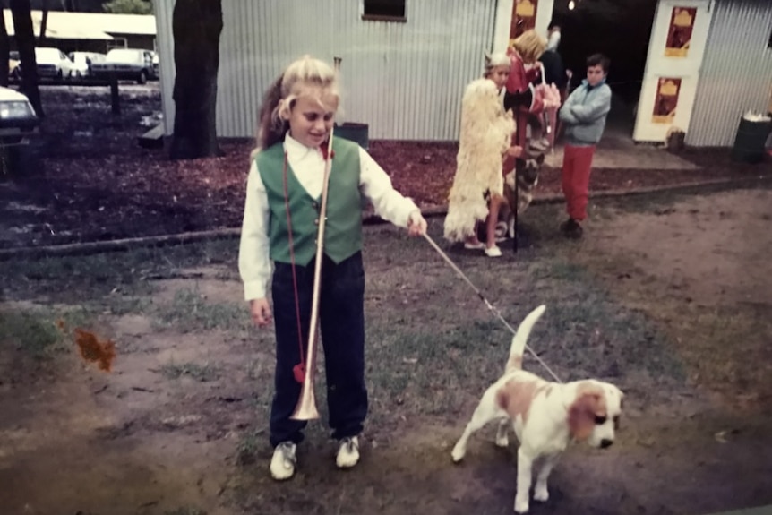 A young Rebel Wilson stands with a dog on a lead.