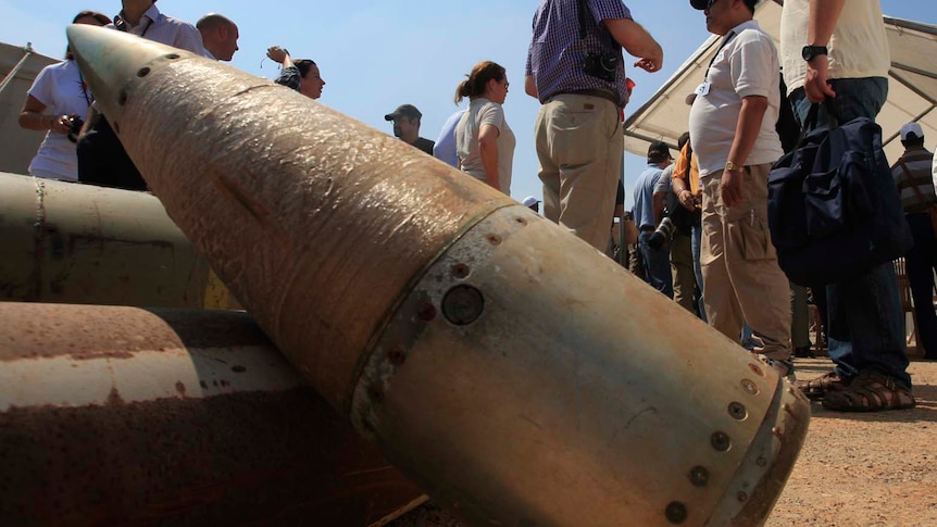 People standing behind cluster bomb shells. 