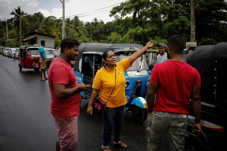 Three men look at a woman standing next to an auto-rickshaw taxi