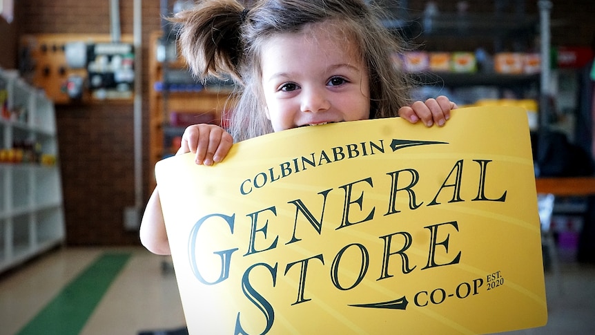 A little boy bites into a bright yellow sign with the words Colbinabbin General Store co-op written on it.