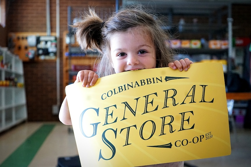 A little boy bites into a bright yellow sign with the words Colbinabbin General Store co-op written on it