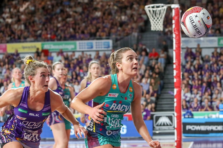 Gabi Simpson and Liz Watson look at a netball as both crouch towards it