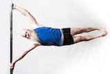 A grey-bearded man in a singlet and shorts holds himself parallel on a pole