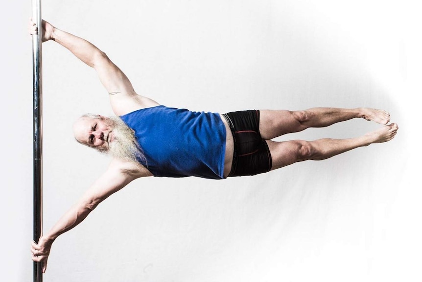 A grey-bearded man in a singlet and shorts holds himself parallel on a pole