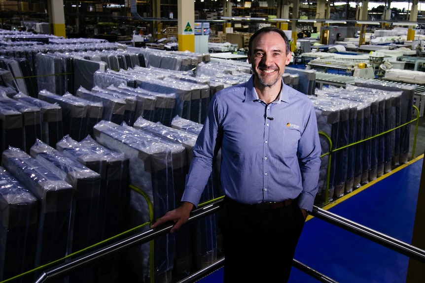 Man in shirt stands in front of mattresses at a mattress factory.