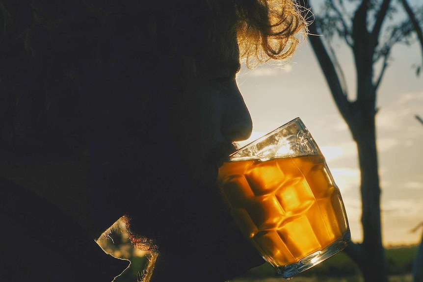 a man sips a beer with the sun setting in the background