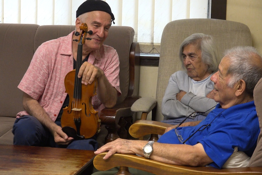 Romano Crivici holding the last violin alongside Harry and Maria Vatiolitis in their living room.