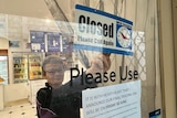A woman with short hair and glasses putting up a closed sign in a door window