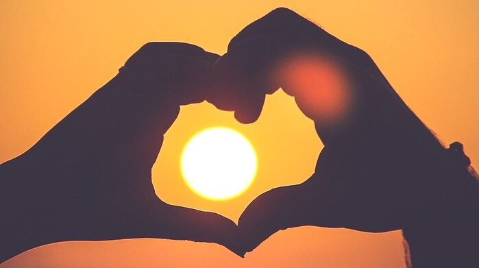 Hands held up in the shape of a heart, framing the sunset.