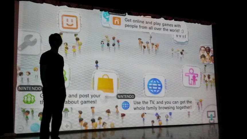 Person standing in front of bright projector screen with various cartoons and captions on it about videogames