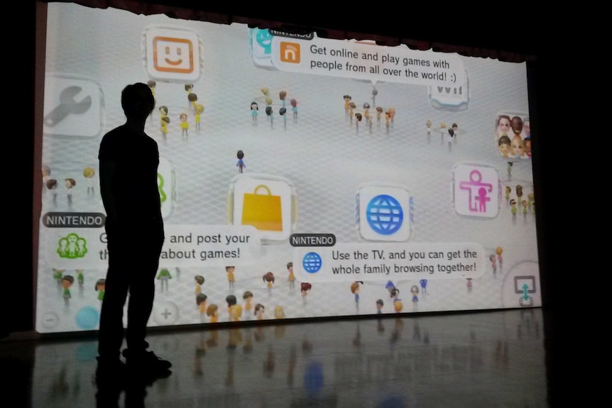 Person standing in front of bright projector screen with various cartoons and captions on it about videogames