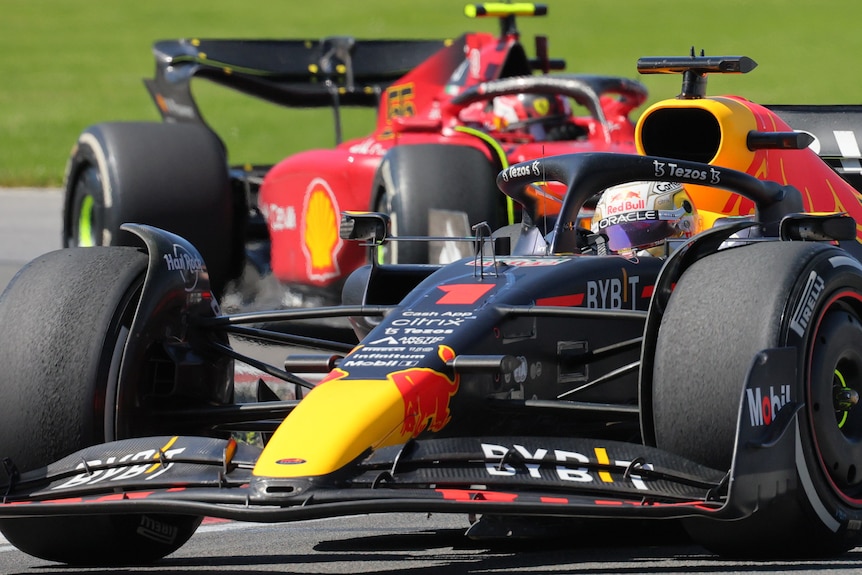 Max Vertsappen in his blue Red Bull F1 car, turning through a corner, ahead of Carlos Sainz in his red Ferrari.