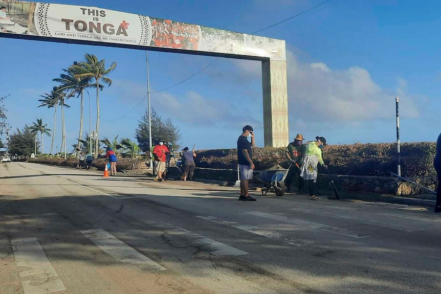 People clear debris off the street in Nuku’alofa under a banner that reads 'this is Tonga'