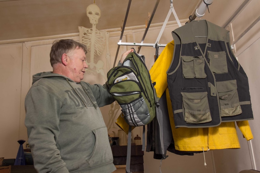 A man looking in a backpack with wet weather gear and jackets with lots of pockets hanging up