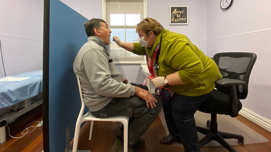 A female doctor takes an oral swab from a male patient.