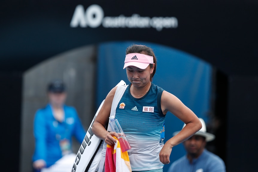 Tennis player Peng Shuai drops her head as she caries her bag under an Australian Open sign.