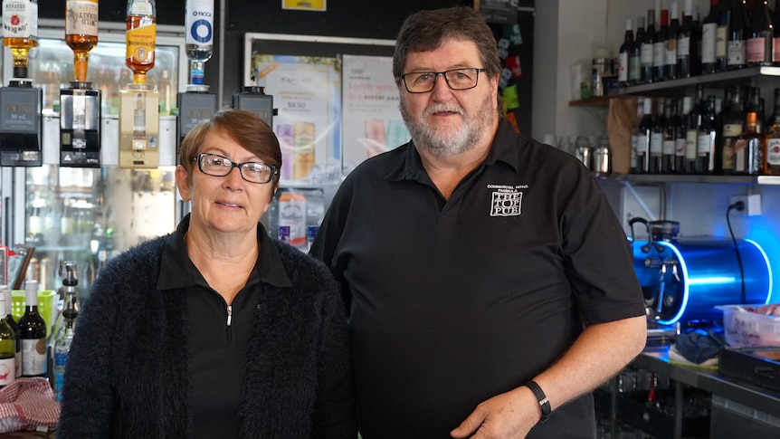 A man and a woman in black clothes and glasses behind a pub bar.