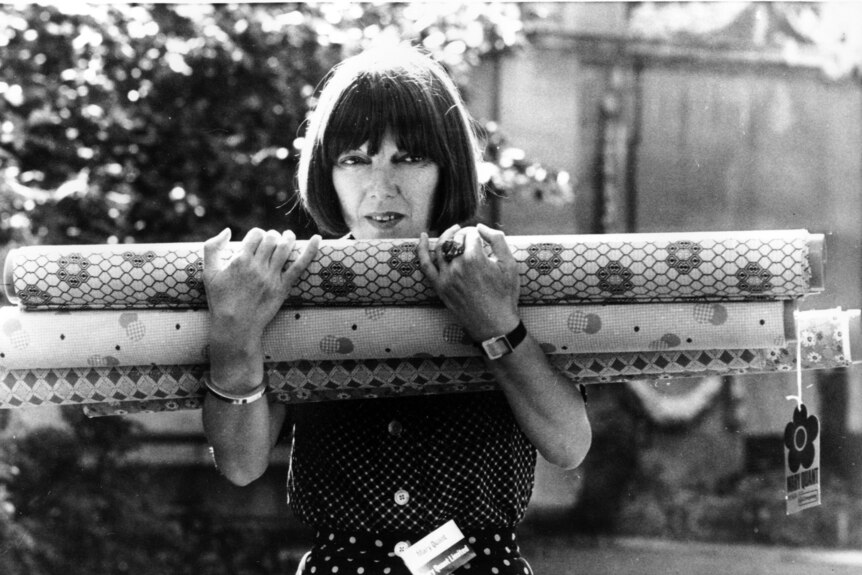 A black and white image of a woman holding rolls of fabric