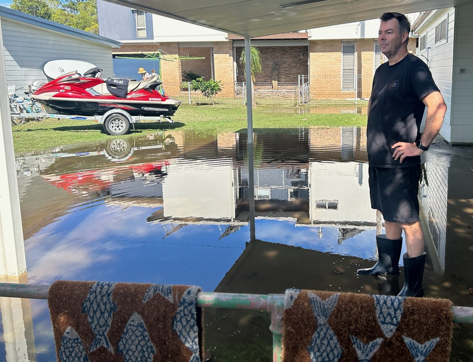 dark haired man wearing dark clothes and gum boots, with hands on hips, standing in puddle of water