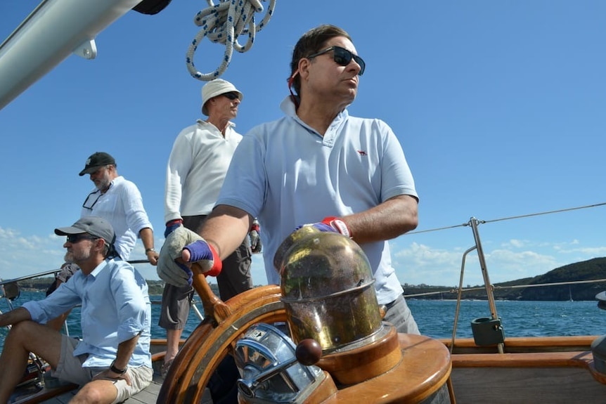 A man steers at a wooden helm.