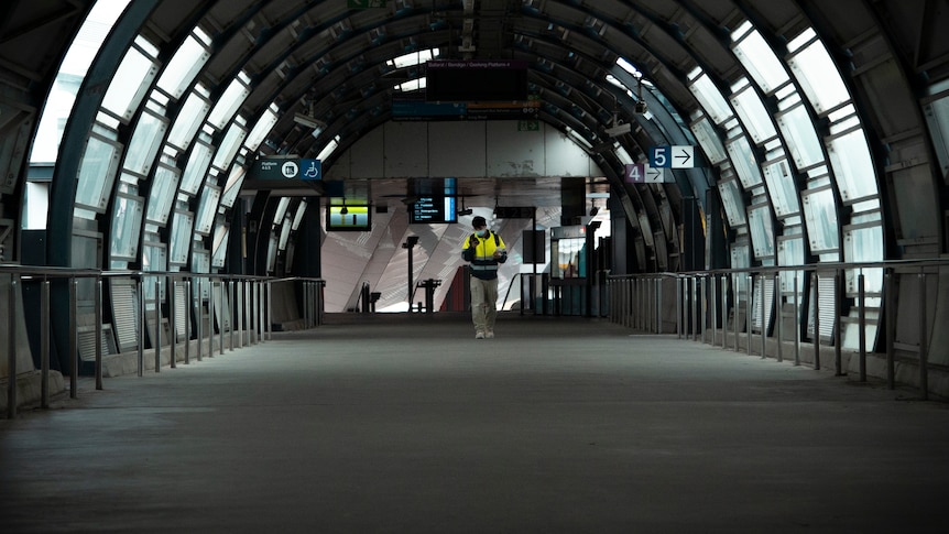 A construction worker in high-vis walks alone through a train station.