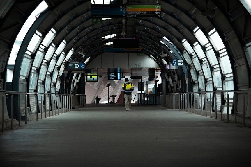 A construction worker in high-vis walks alone through a train station.