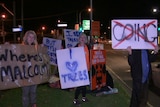 Protesters stand by the road holding signs