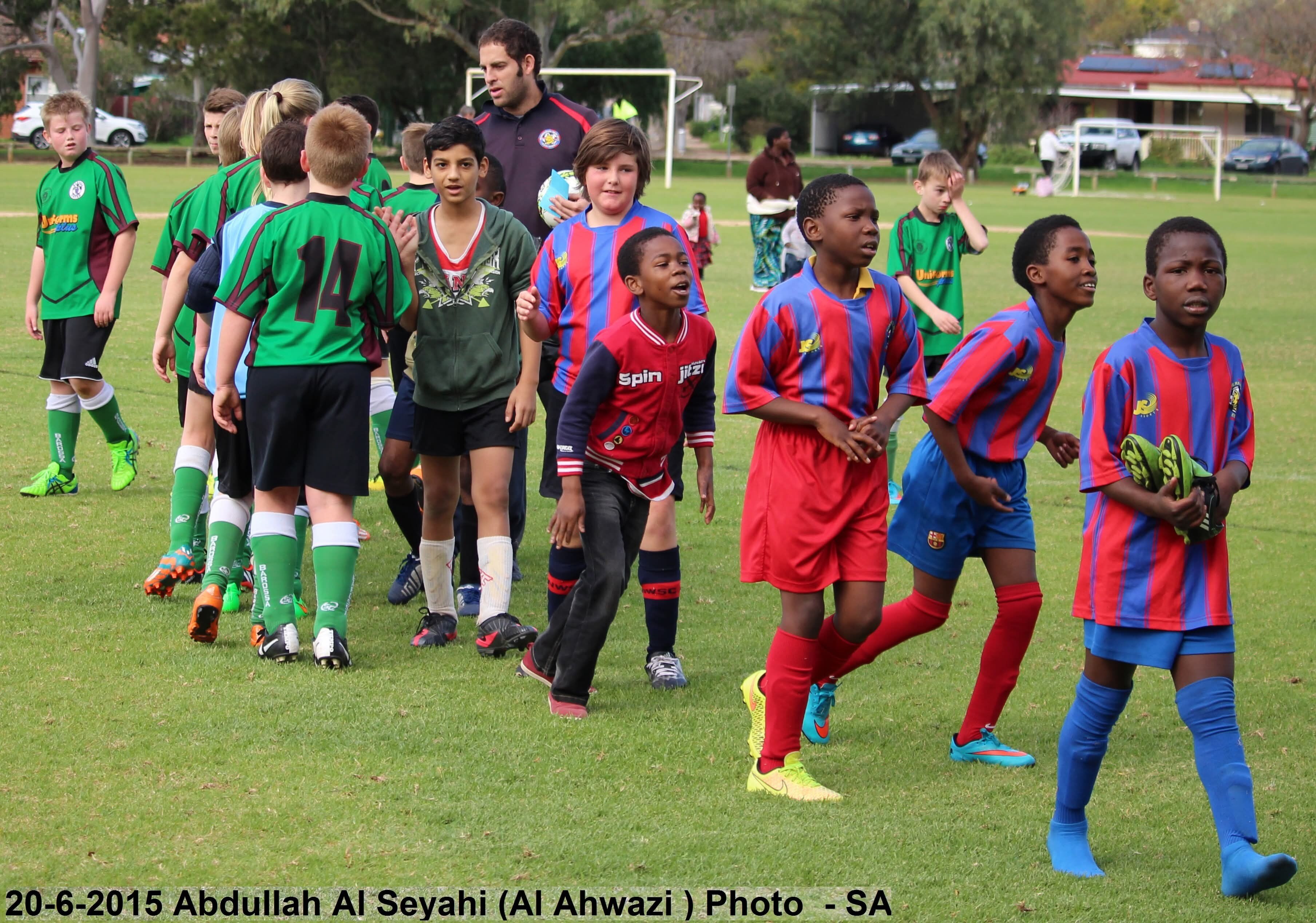 A man stands behind a group of children in soccer uniforms.