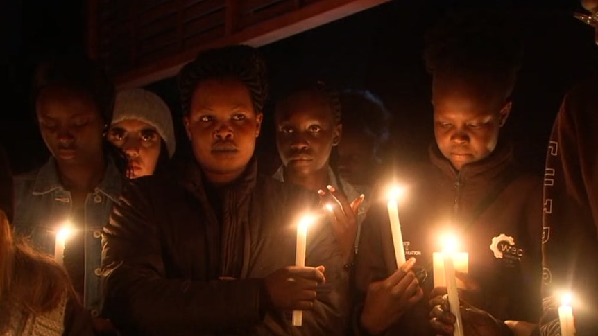 Women hold candles in honour of Abiol Atem Manyang at a vigil.