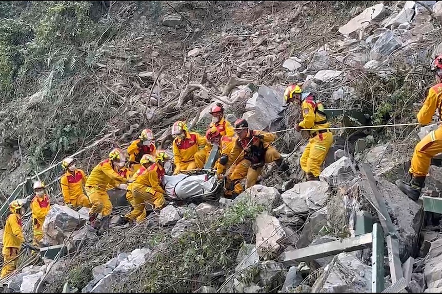 About a dozen men wearing yellow and holding a rope climbing on the side of a mountain