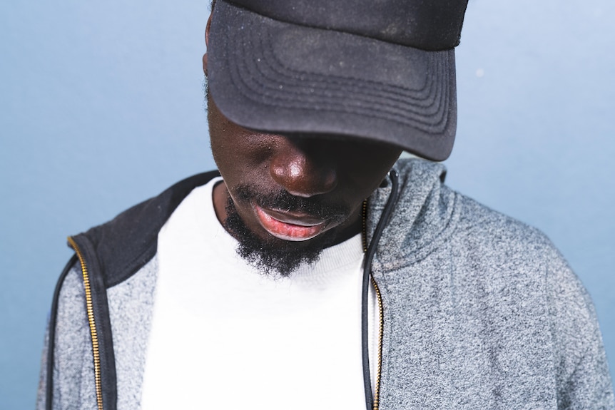 A close up picture of an African man looking down, his face covered by a baseball cap