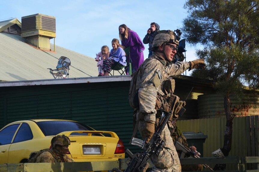 A local family watches on as US and Aussie troops fight a mock battle