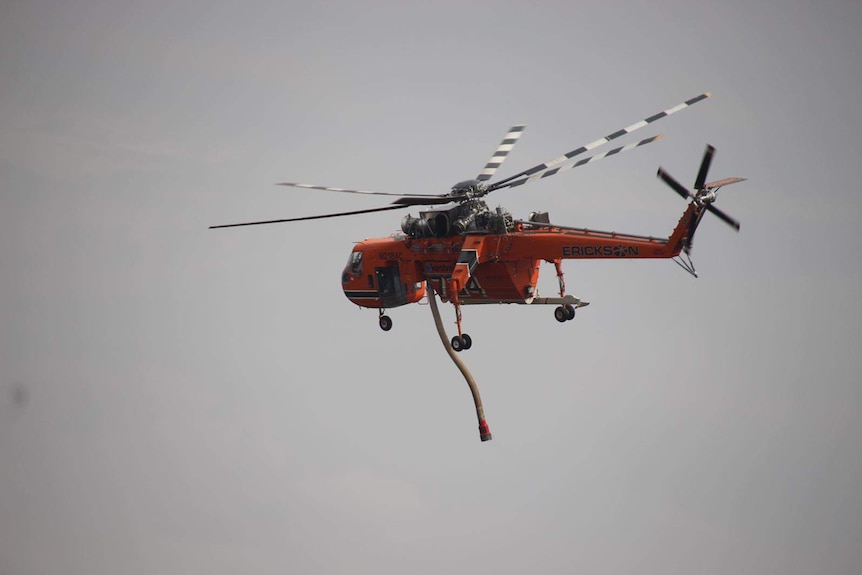 An orange helicopter flying in the air