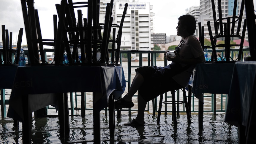 Man sits in flooded restaurant in downtown Bangkok.