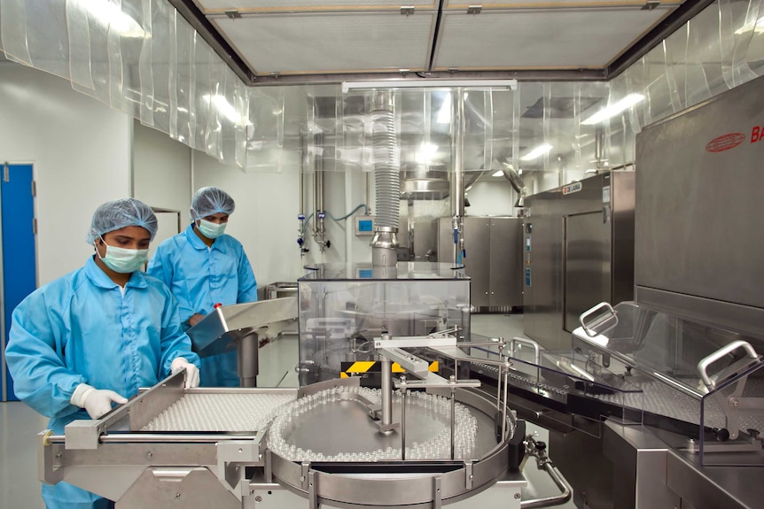 Two men in blue lab coats examine a piece of factory machinery