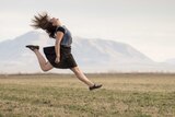 A woman jumping for joy in a field of grass.