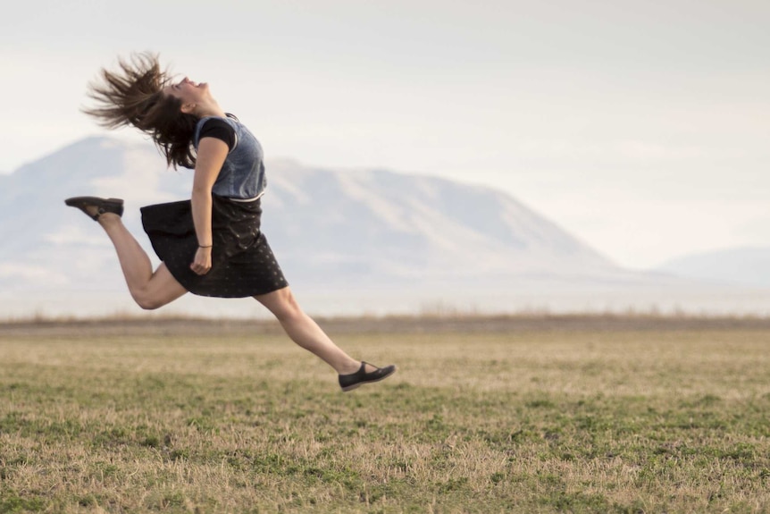 A woman jumping for joy in a field of grass.