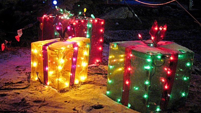 Christmas light presents sit outside under a lit up tree.