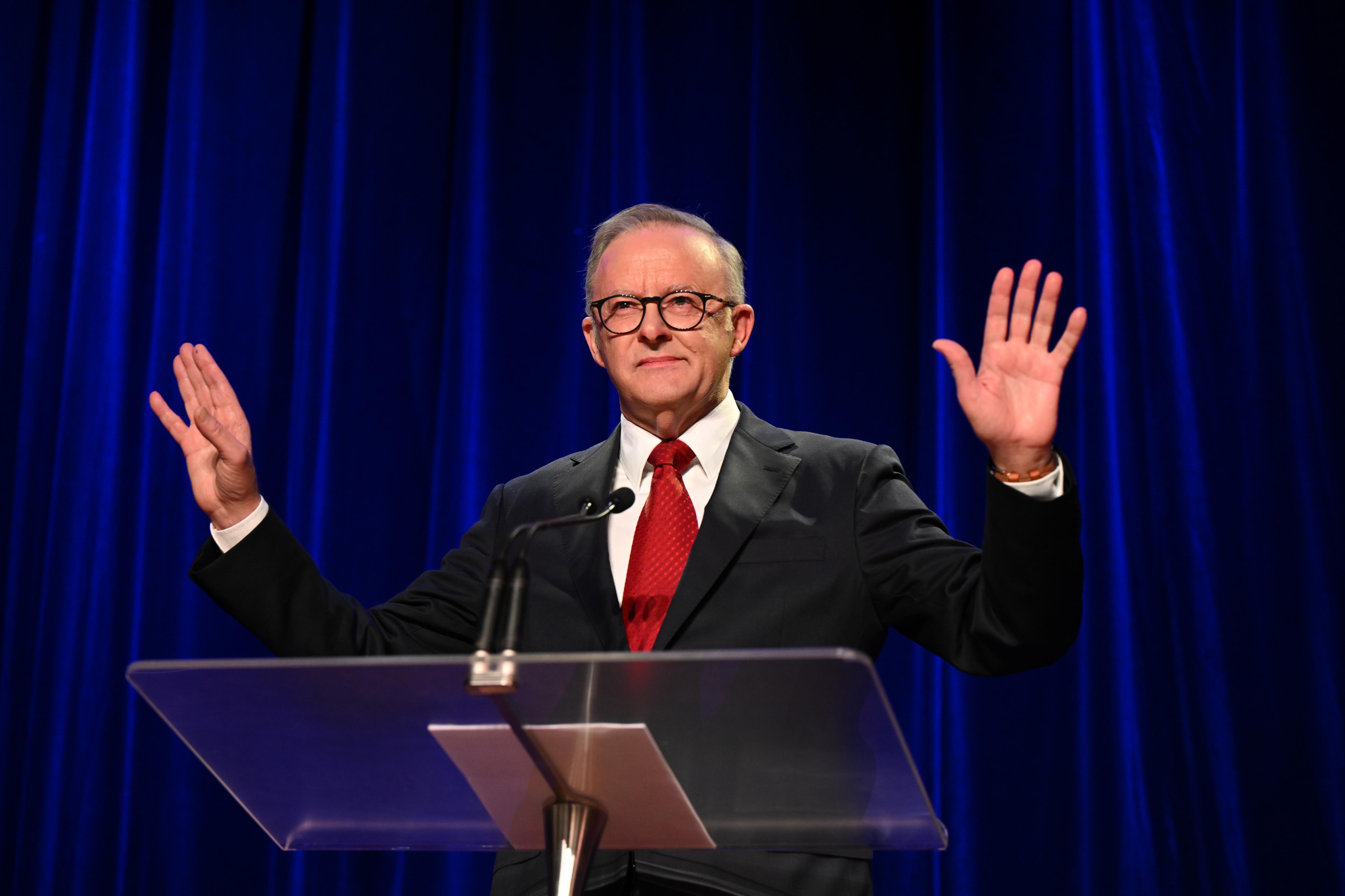 Anthony Albanese holds up his hands to calm the crowd.