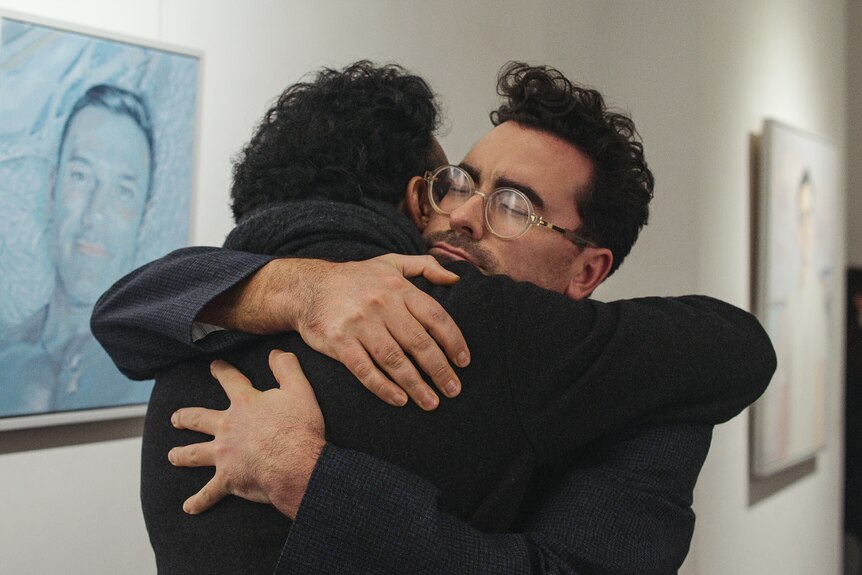 A film still of Himesh Patel and Daniel Levy hugging closely, Patel facing away from the camera, Levy with his eyes closed.