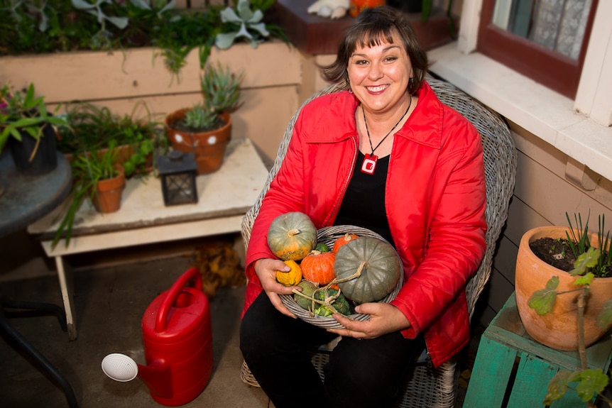 Gardener Lou Ridsdale sitting in a chair holding a basket full of vegetables grown in her garden.