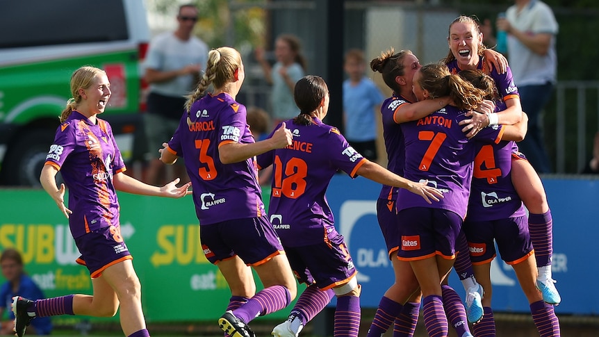 A soccer team wearing purple and orange hug and celebrate during a match