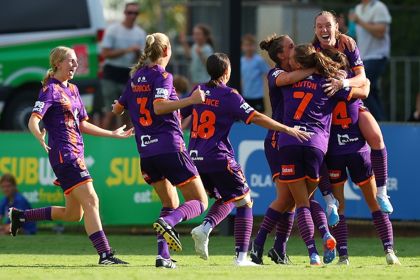 A soccer team wearing purple and orange hug and celebrate during a match