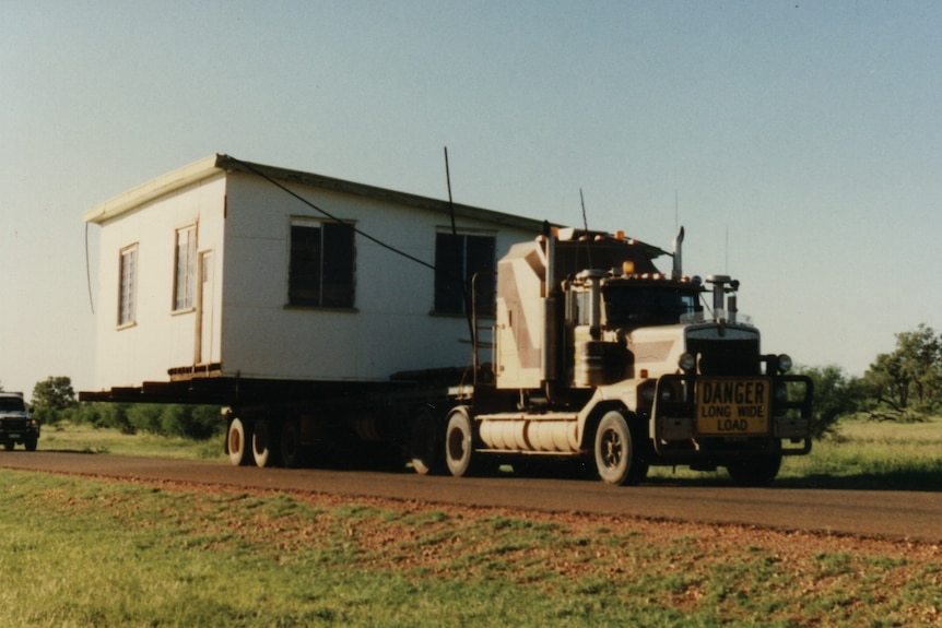 A truck with a small house on its trailer drives on an outback road