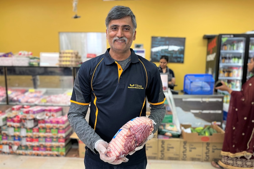 A man holding a packaged piece of meat and smiling, inside a butchery business.