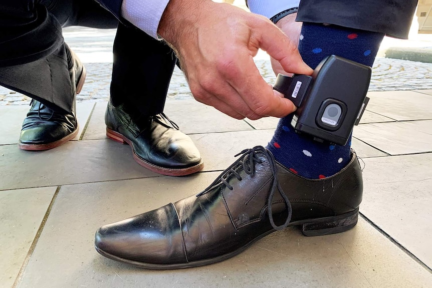 Close-up of hands attaching a tracking device around a man's ankle in Brisbane.