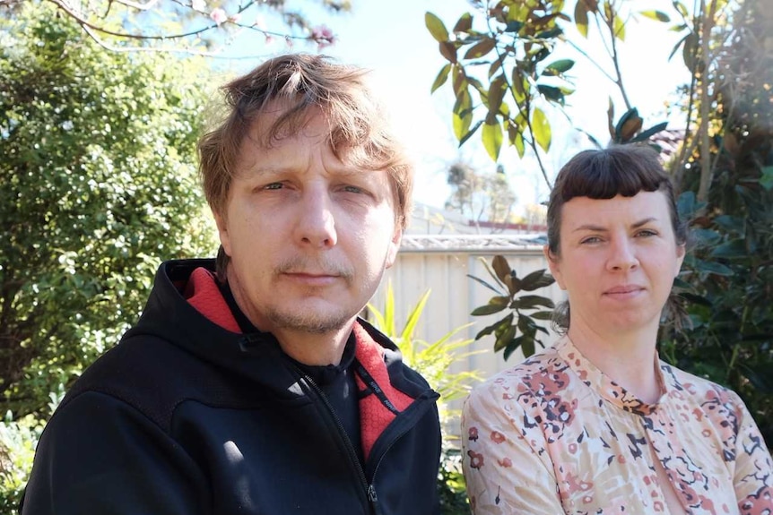 A man and a woman are sitting next to each other and looking into the camera with serious faces