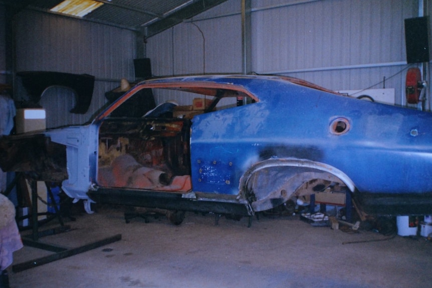 An old photograph of a run down car elevated, painted blue.